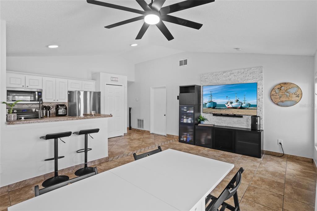 An open-concept living and dining area features tile flooring, a kitchen island, and a television — 2239 SANTA LUCIA STREET, KISSIMMEE, FL