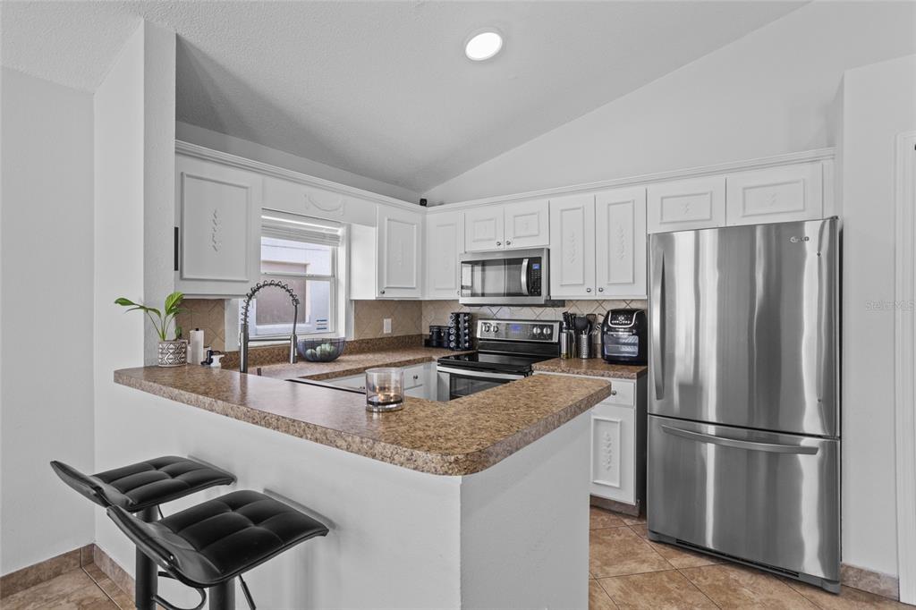 A kitchen with white cabinets, stainless steel appliances, and a brown speckled countertop breakfast bar — 2239 SANTA LUCIA STREET, KISSIMMEE, FL