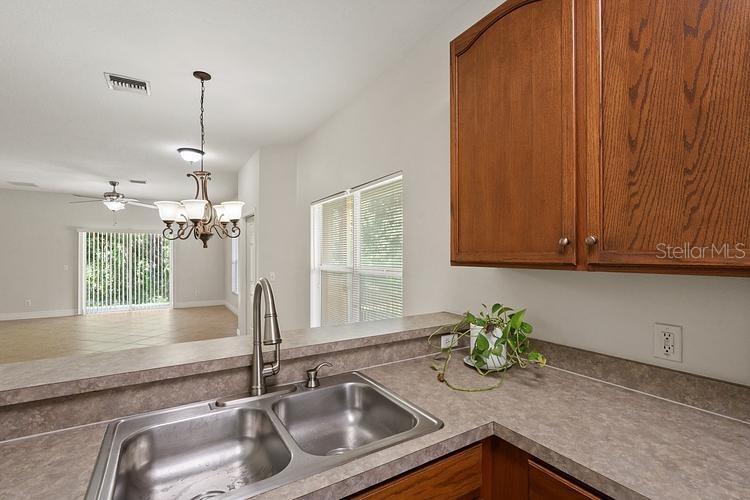 A kitchen sink and countertop overlook an open living area with a chandelier and blinds — 20221 VINTAGE OAKS PLACE, TAMPA, FL