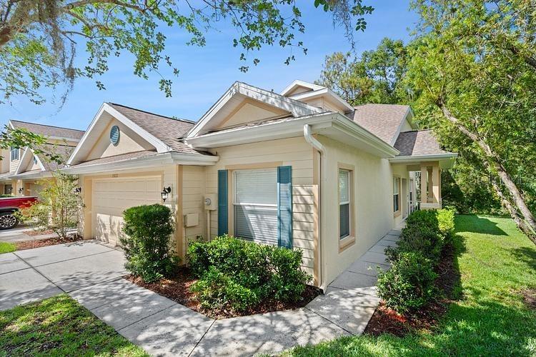 A beige house with a gabled roof, a garage, and green landscaping under a blue sky — 20221 VINTAGE OAKS PLACE, TAMPA, FL