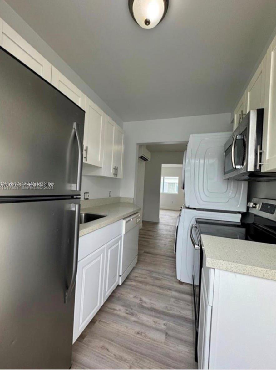 A galley kitchen features white cabinets, light countertops, stainless steel appliances, and wood-look flooring — MIAMI BEACH, FL