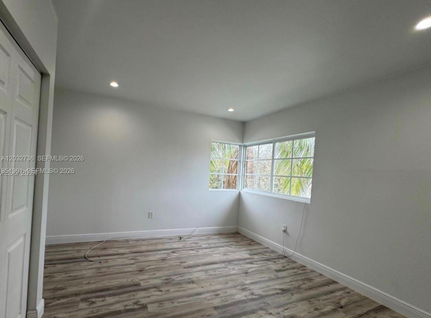 An empty room features light-colored walls, wood-look flooring, recessed lighting, and a corner window — MIAMI BEACH, FL