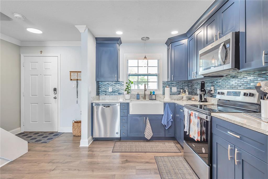 A kitchen features blue cabinets, a farmhouse sink, stainless steel appliances, and a tiled backsplash — 5172 COQUINA KEY DRIVE SE, ST PETERSBURG, FL