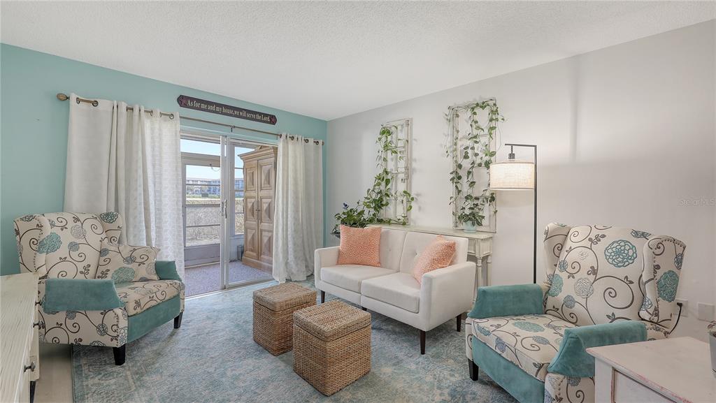 A living room features two patterned armchairs, a white loveseat, and a sliding glass door — 3845 LAKE BAYSHORE DRIVE UNIT F103, BRADENTON, FL