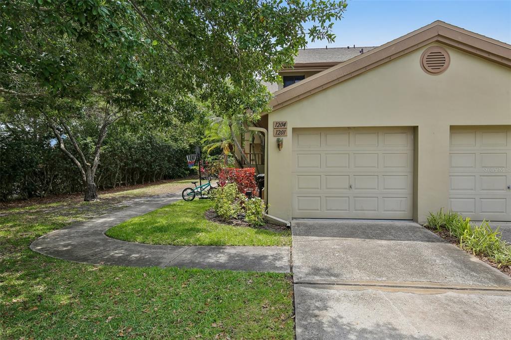 A tan residential building with two garage doors and a concrete walkway in the front — 3058 LANDMARK BOULEVARD UNIT 1204, PALM HARBOR, FL