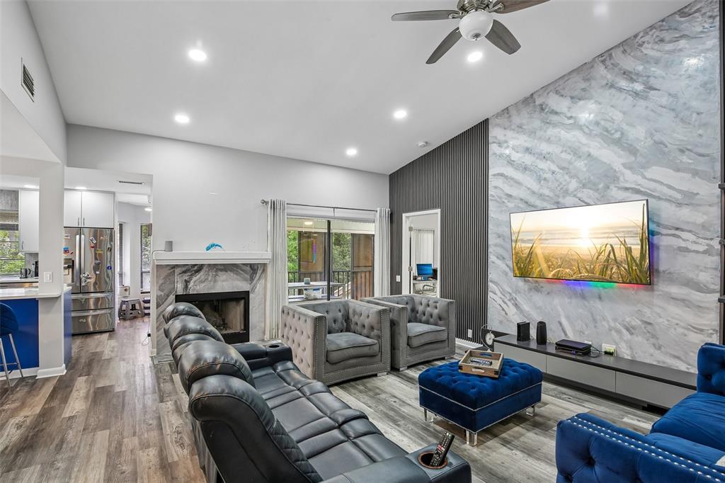 A living room features a marble-tiled accent wall with a television, fireplace, and modern furniture — 3058 LANDMARK BOULEVARD UNIT 1204, PALM HARBOR, FL