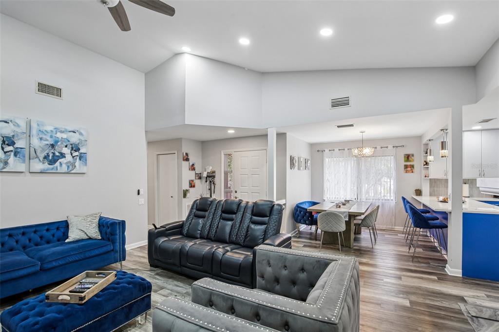 An open-concept living and dining area features vaulted ceilings, blue furniture, and wood-look flooring — 3058 LANDMARK BOULEVARD UNIT 1204, PALM HARBOR, FL