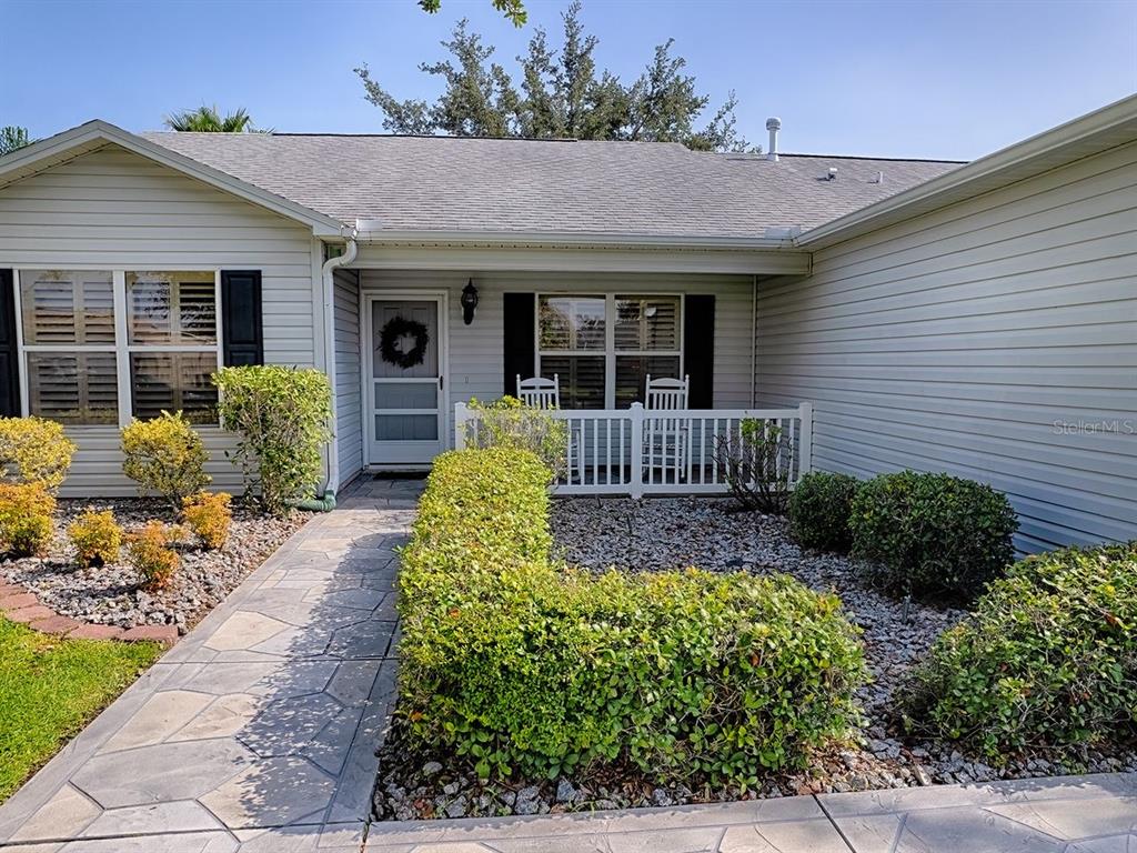A light-colored house exterior features a stone walkway, a small porch, and manicured landscaping — 2189 CRAWFORD COURT, THE VILLAGES, FL