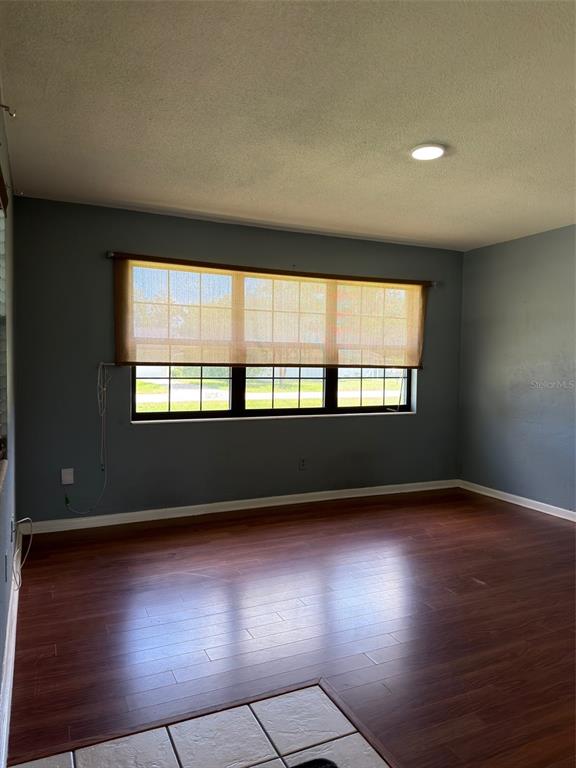 An empty room with blue walls, dark wood flooring, and a large window with shades — 21160 SW HONEYSUCKLE STREET, DUNNELLON, FL