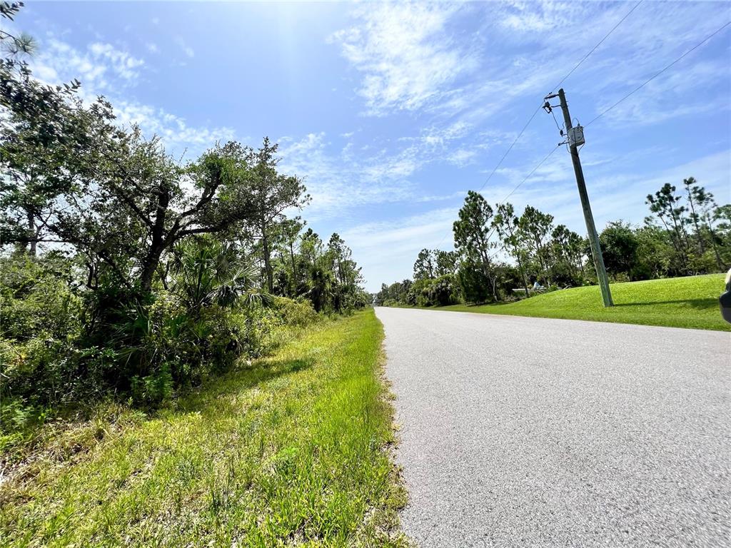 A paved road runs alongside a grassy shoulder with trees and a utility pole — 13377 JOHANNES AVENUE, PORT CHARLOTTE, FL