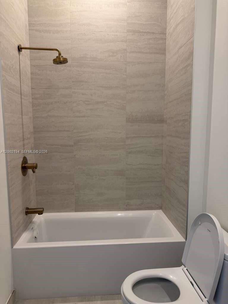 A bathroom features a white bathtub with gold fixtures against light-colored, horizontal-patterned wall tiles — 77 SE 5th street # 1011, Miami FL 33131, MIAMI, FL