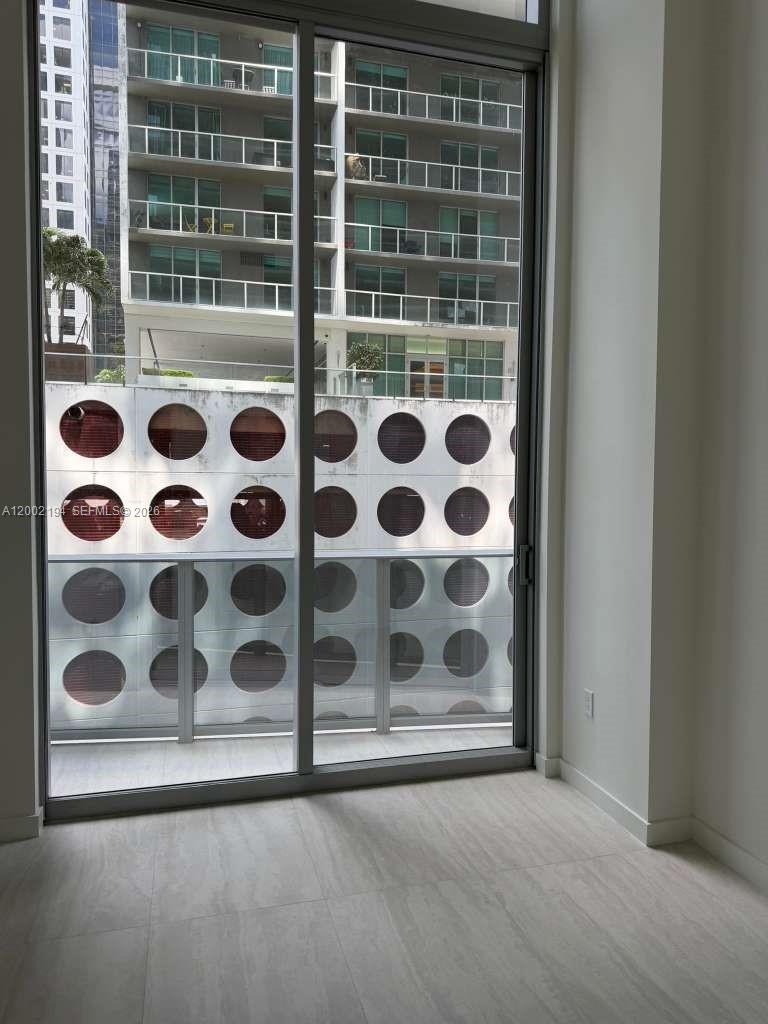 A room with light-colored flooring features a large sliding glass door overlooking a parking structure — 77 SE 5th street # 1011, Miami FL 33131, MIAMI, FL