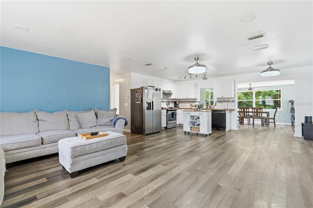 An open-concept living room and kitchen featuring light wood floors and a blue accent wall — 1609 CLEARVIEW AVENUE, CLEARWATER, FL