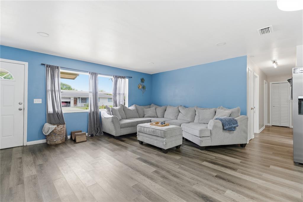 A living room features a large gray sectional sofa, blue walls, and wood-look flooring — 1609 CLEARVIEW AVENUE, CLEARWATER, FL