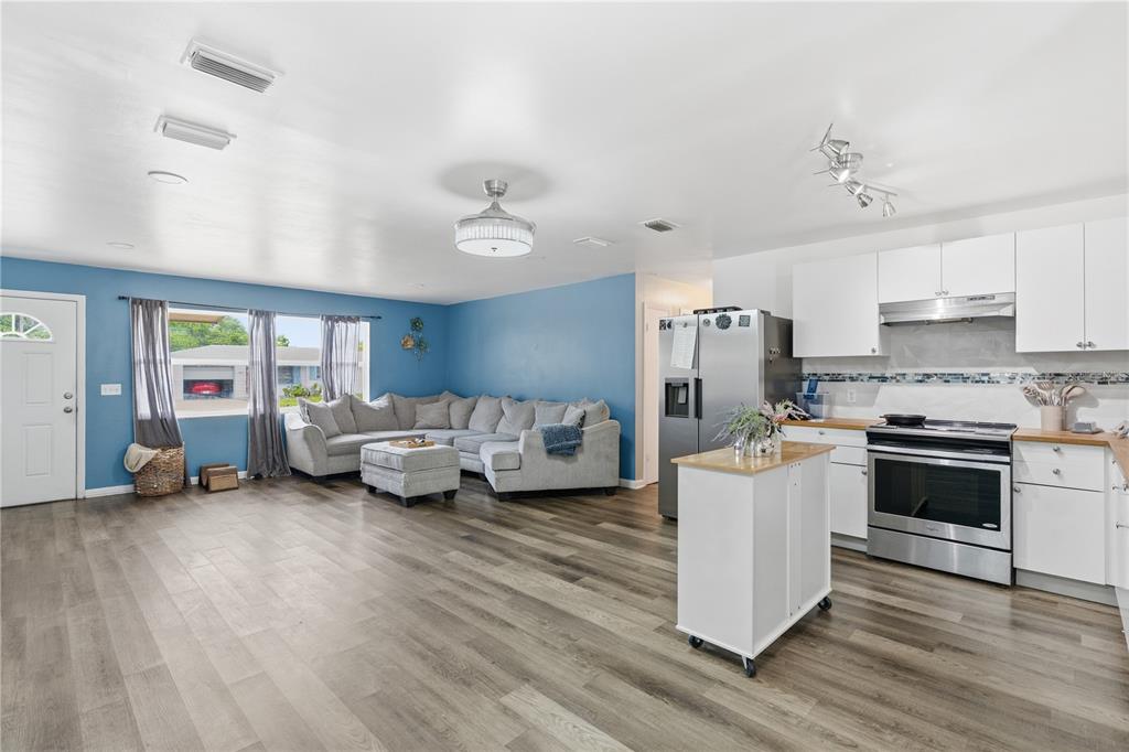 An open-concept living room and kitchen with blue walls, gray flooring, and white cabinetry — 1609 CLEARVIEW AVENUE, CLEARWATER, FL