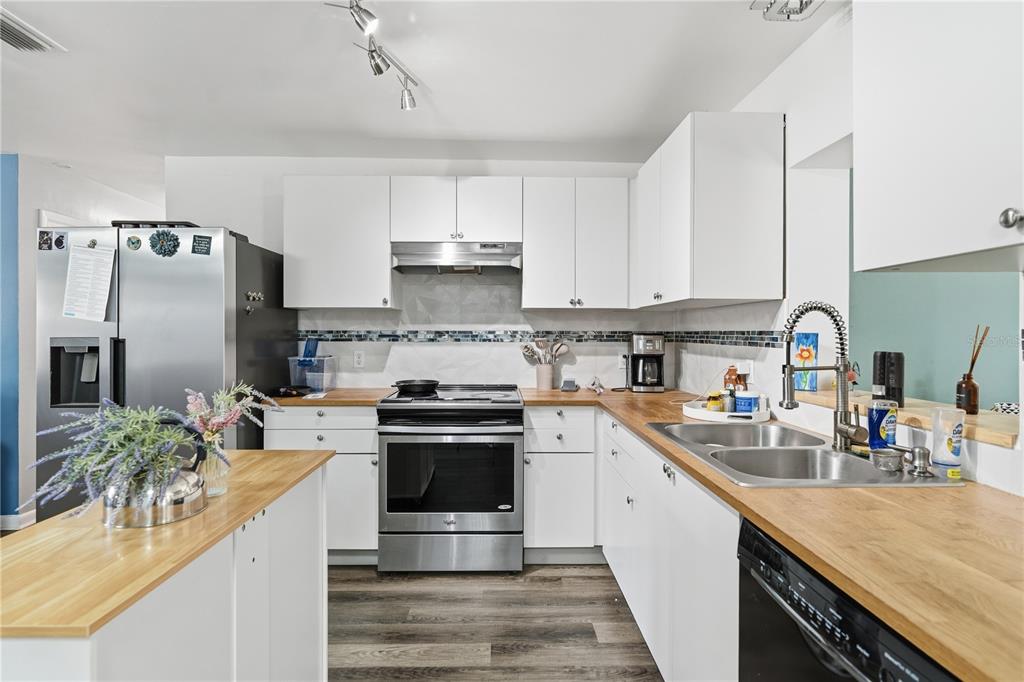A kitchen features white cabinets, butcher block countertops, stainless steel appliances, and wood-look flooring — 1609 CLEARVIEW AVENUE, CLEARWATER, FL