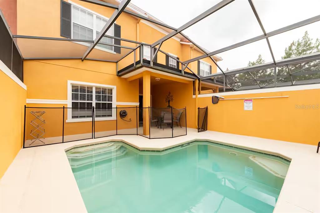 A screened-in swimming pool sits on a patio next to a two-story yellow house — 8977 COCO PALM ROAD, KISSIMMEE, FL