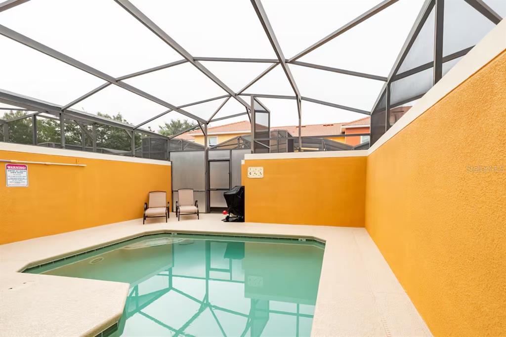 A screened-in swimming pool area features yellow walls, two chairs, and a concrete deck — 8977 COCO PALM ROAD, KISSIMMEE, FL