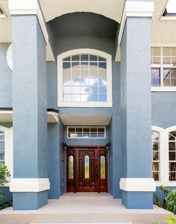 The exterior of a blue house features a large arched window above a wooden front door — 1153 OAK TREE CIRCLE, ALTAMONTE SPRINGS, FL