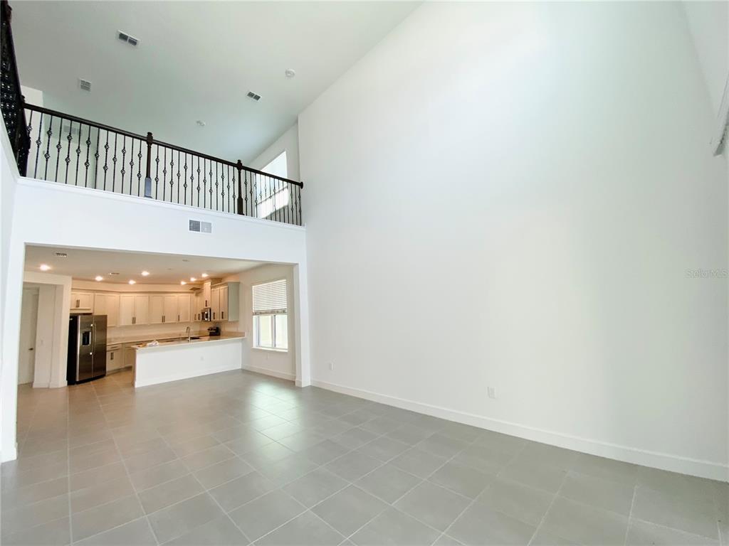 A high-ceilinged living area with tile flooring overlooks an open kitchen with white cabinets — 2348 KESTREL PERCH PLACE, WINTER PARK, FL