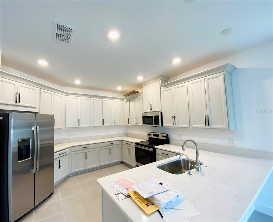 A modern kitchen features white cabinets, stainless steel appliances, and light-colored quartz countertops — 2348 KESTREL PERCH PLACE, WINTER PARK, FL