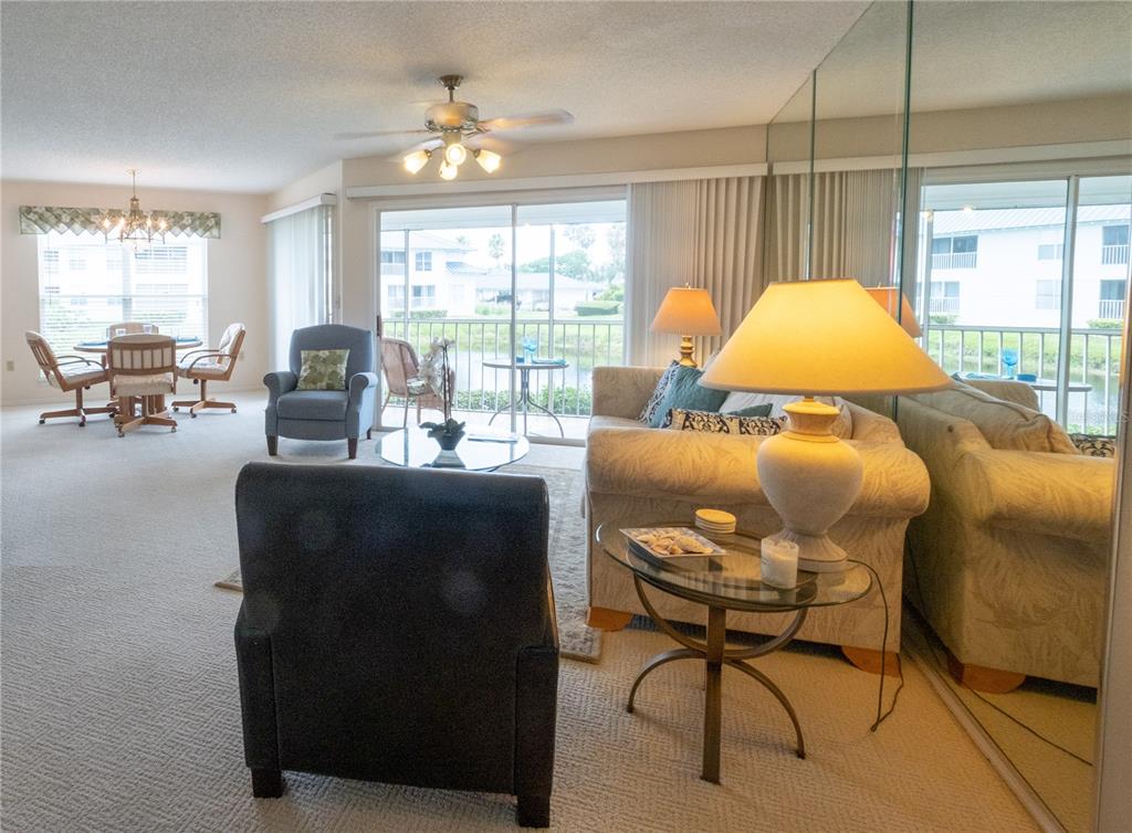 A living room with carpeted floors, a ceiling fan, and a sliding glass door to a balcony — 831 AUDUBON DRIVE UNIT 831, BRADENTON, FL