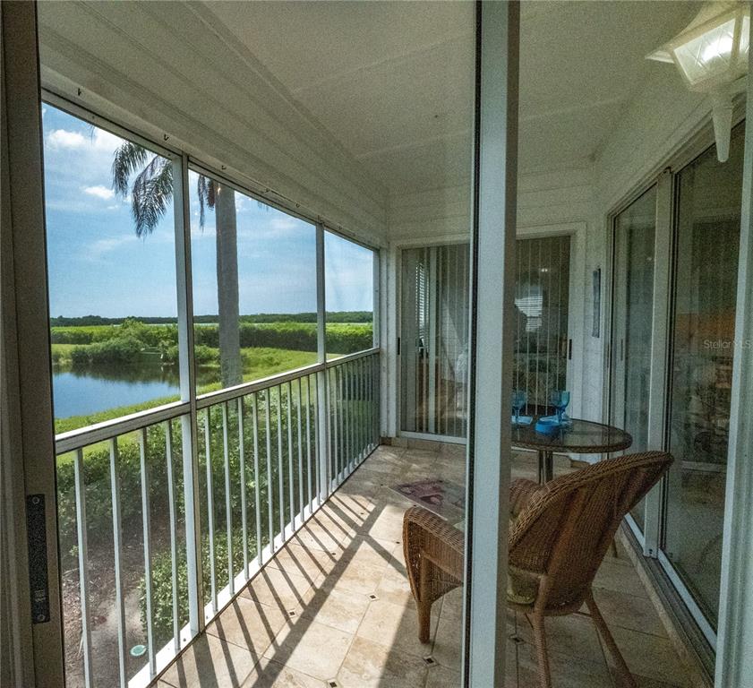A screened balcony features tiled flooring, wicker furniture, and a view of a pond — 831 AUDUBON DRIVE UNIT 831, BRADENTON, FL