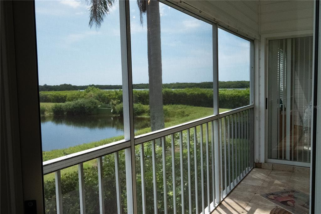A screened-in balcony with tile flooring overlooks a pond and a line of trees — 831 AUDUBON DRIVE UNIT 831, BRADENTON, FL