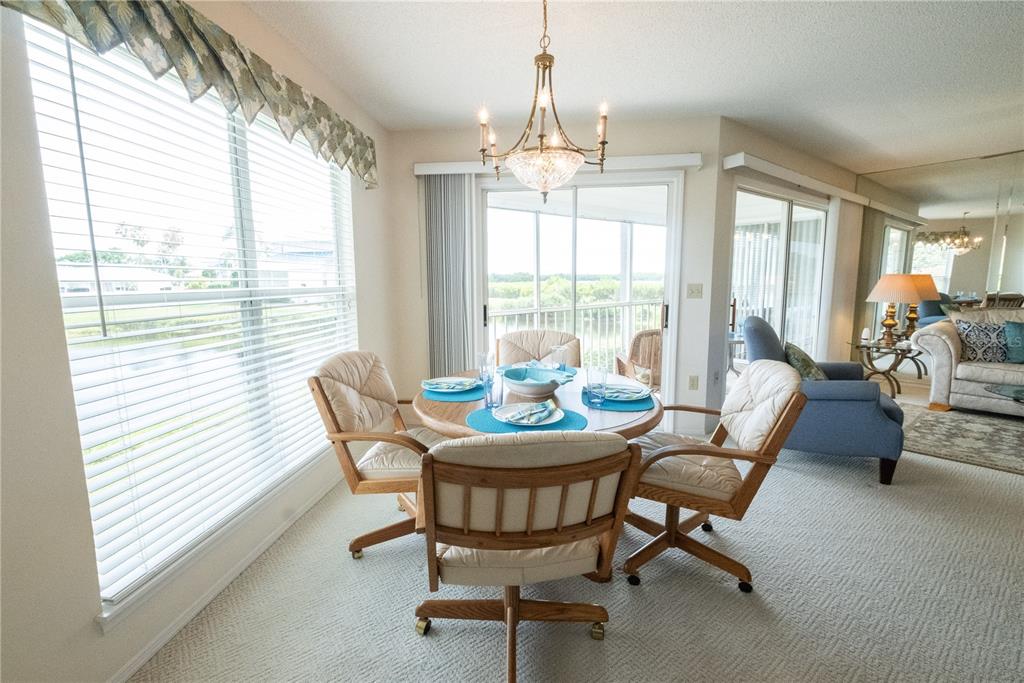 A dining area with a round table, four chairs, a chandelier, and large windows — 831 AUDUBON DRIVE UNIT 831, BRADENTON, FL
