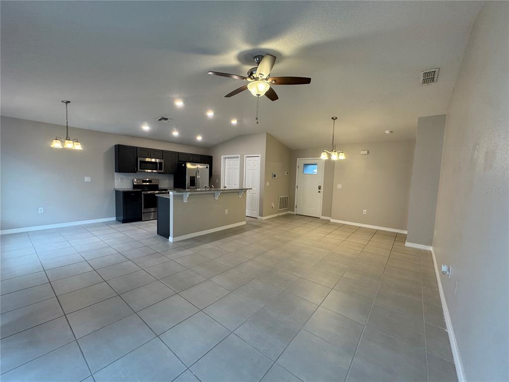 An open-concept kitchen and living area features dark cabinetry, tile flooring, and a ceiling fan — 350 W ASTER COURT, POINCIANA, FL