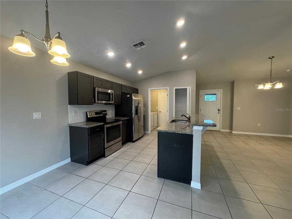 A kitchen features dark cabinets, granite countertops, stainless steel appliances, and light-colored tile flooring — 350 W ASTER COURT, POINCIANA, FL