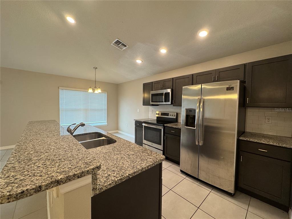 A kitchen with dark cabinets, granite countertops, stainless steel appliances, and tile flooring — 350 W ASTER COURT, POINCIANA, FL
