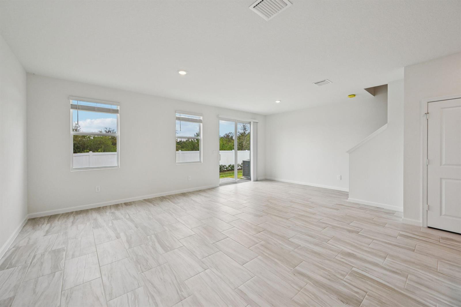 An empty living room features white walls, light wood-look tile flooring, and a sliding glass door — 568 Salisbury Circle, Fort Pierce FL 34982, FORT PIERCE, FL