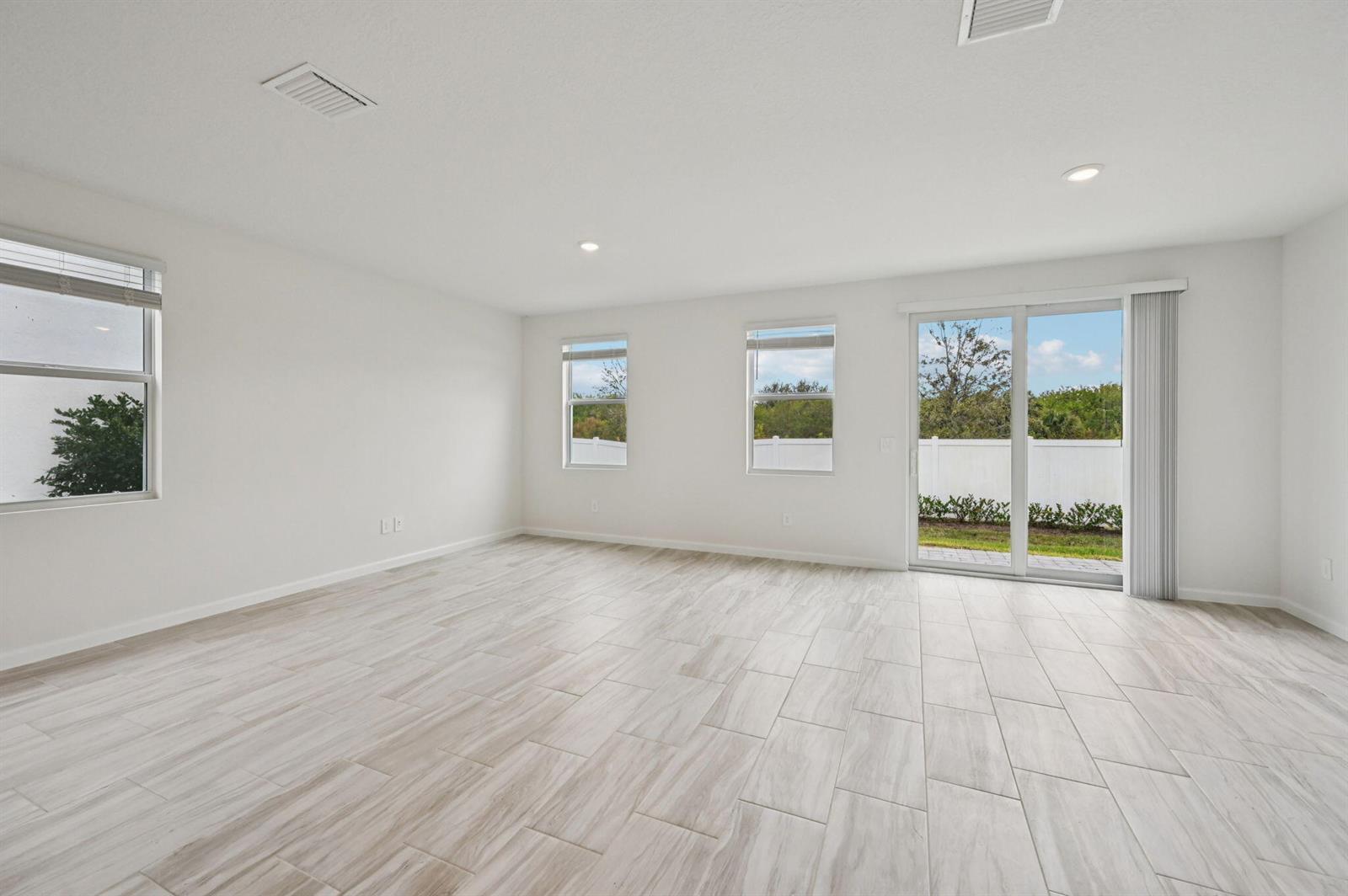An empty living room features white walls, light wood-look tile flooring, and sliding glass doors — 568 Salisbury Circle, Fort Pierce FL 34982, FORT PIERCE, FL