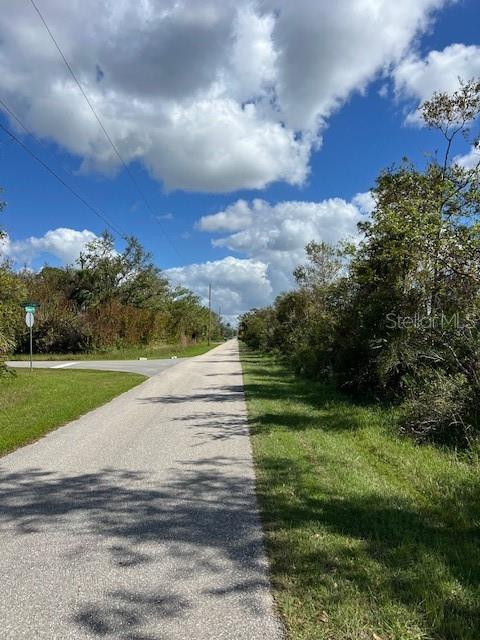 A paved road stretches into the distance, flanked by grassy shoulders and dense trees — 13100 ELEANOR AVENUE, PORT CHARLOTTE, FL