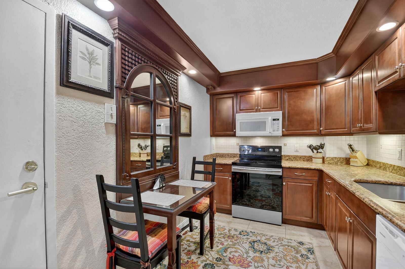 A kitchen with dark wood cabinets, granite countertops, a small dining table, and a mirror — 3450 S Ocean Boulevard # 520, Palm Beach FL 33480, PALM BEACH, FL