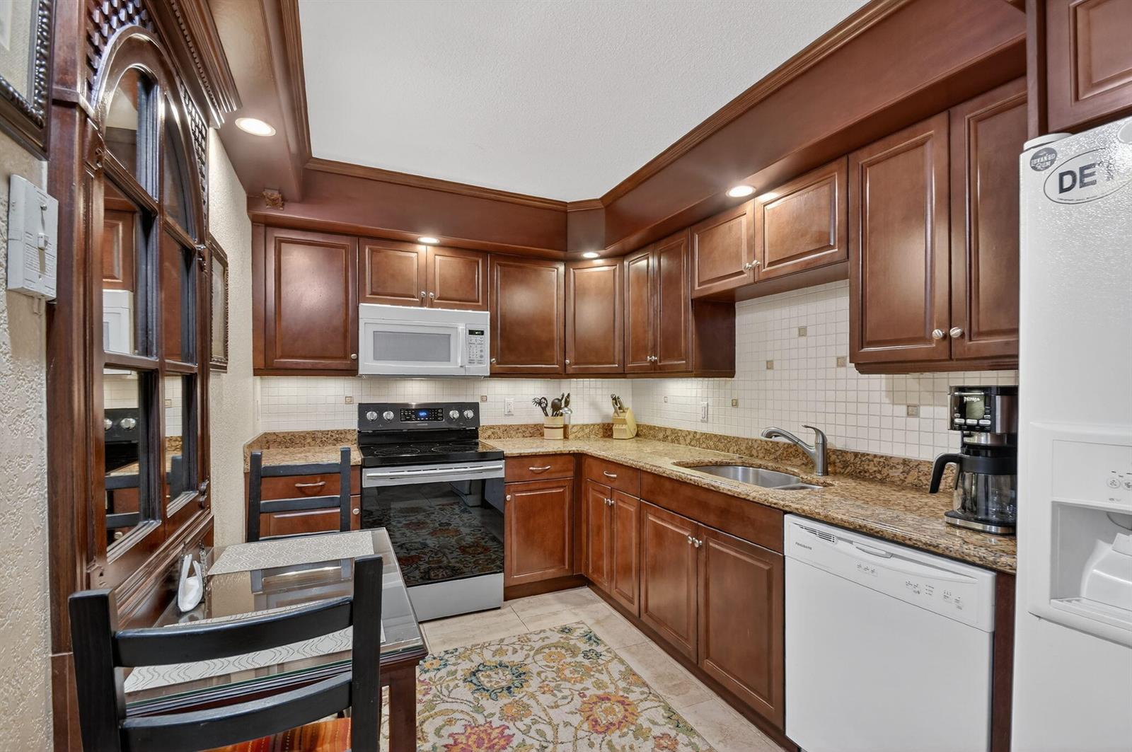A kitchen features dark wood cabinets, granite countertops, stainless steel appliances, and a small dining table — 3450 S Ocean Boulevard # 520, Palm Beach FL 33480, PALM BEACH, FL