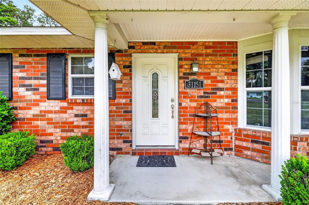 A brick house exterior features a white front door, two columns, and a small porch — 31151 DEAL DRIVE, MOUNT PLYMOUTH, FL