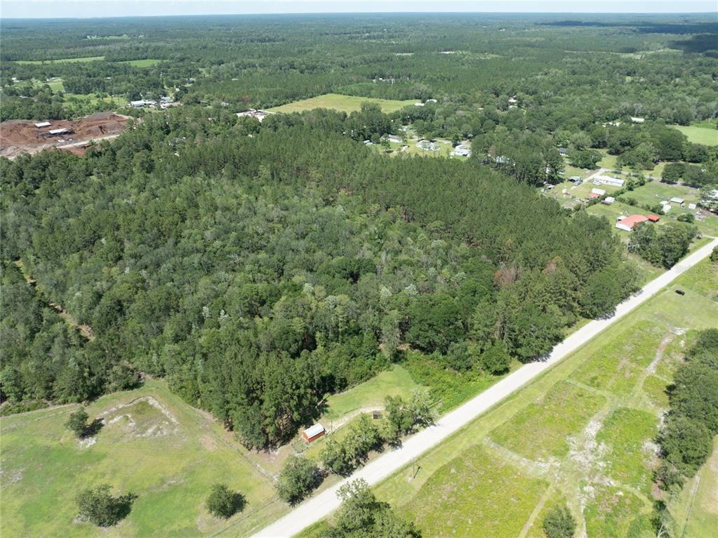 An aerial view shows a wooded lot bordering a road with a small red building — NW 185TH STREET, STARKE, FL
