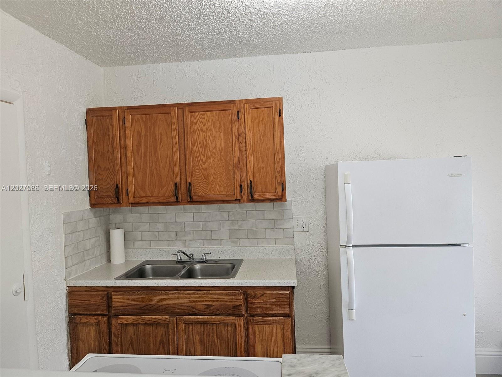 A kitchen features wood cabinets, a stainless steel sink, a tiled backsplash, and a refrigerator — 709 NE 4th Ct # 2, Hallandale Beach FL 33009, HALLANDALE BEACH, FL
