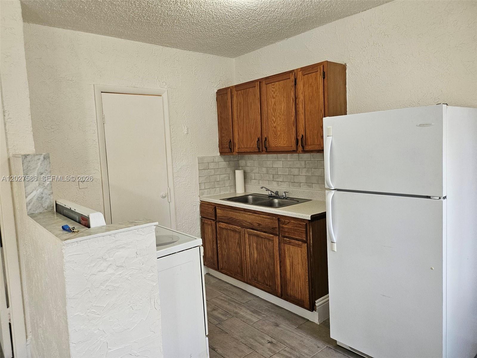 A small kitchen features wooden cabinets, a white refrigerator, and a stainless steel sink — 709 NE 4th Ct # 2, Hallandale Beach FL 33009, HALLANDALE BEACH, FL