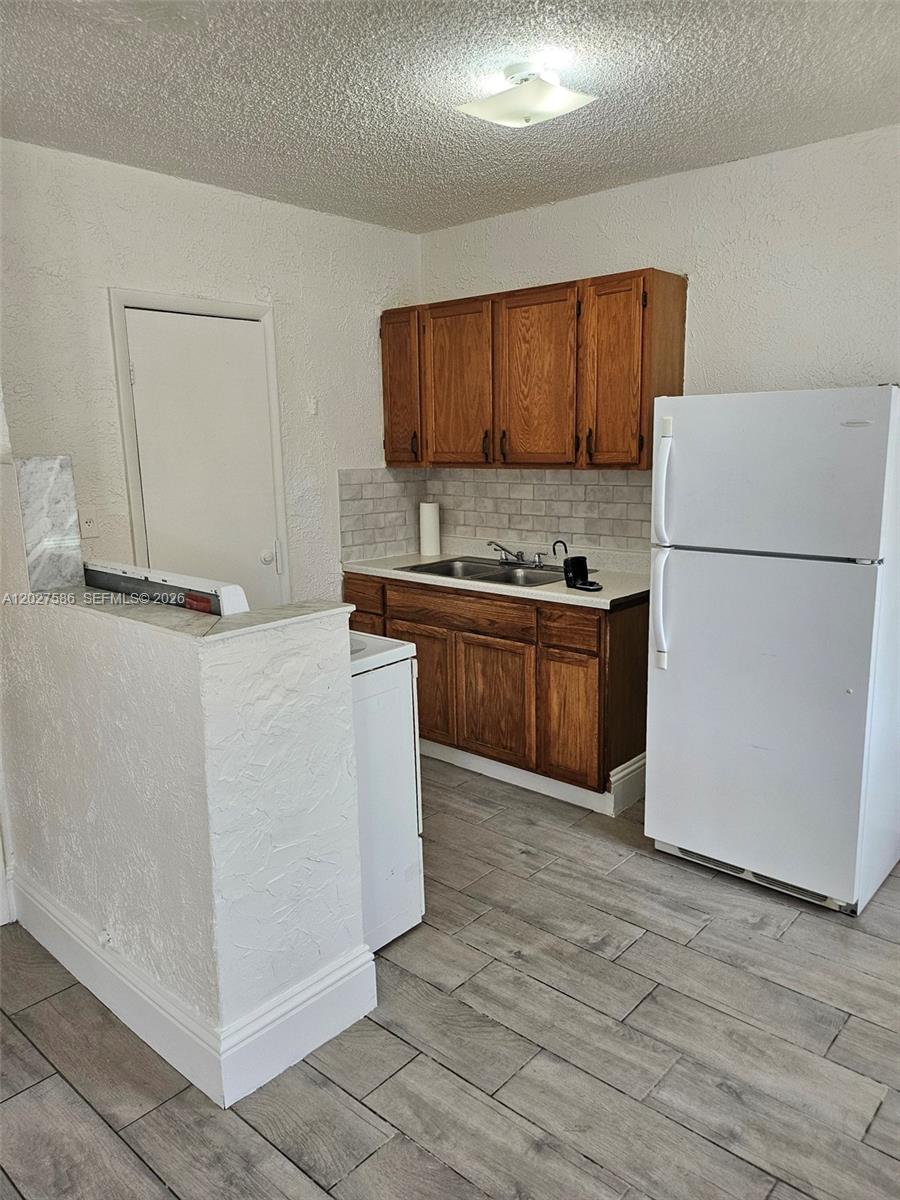 A small kitchen features wood cabinets, a white refrigerator, and light-colored tile flooring — 709 NE 4th Ct # 2, Hallandale Beach FL 33009, HALLANDALE BEACH, FL