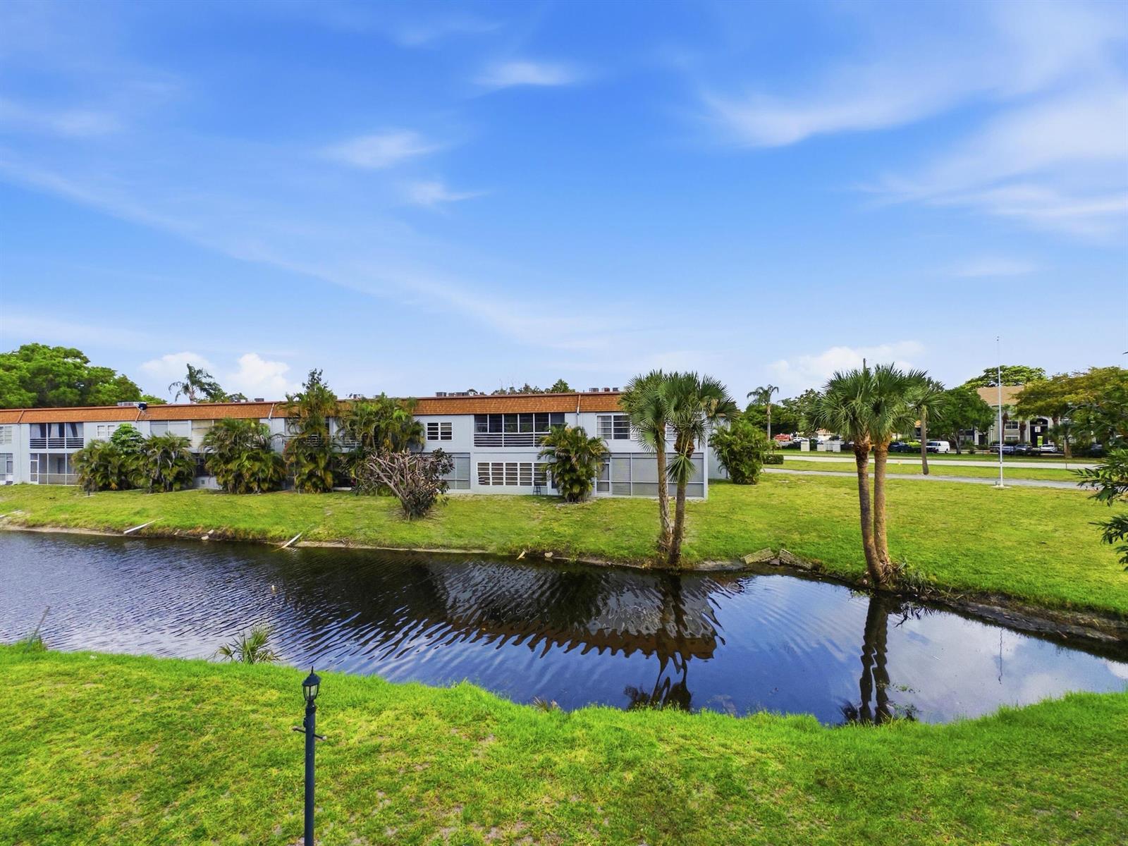 A two-story apartment building sits behind a small canal with palm trees and grass — 6289 Lear Drive # 206, Lake Worth FL 33462, LAKE WORTH, FL