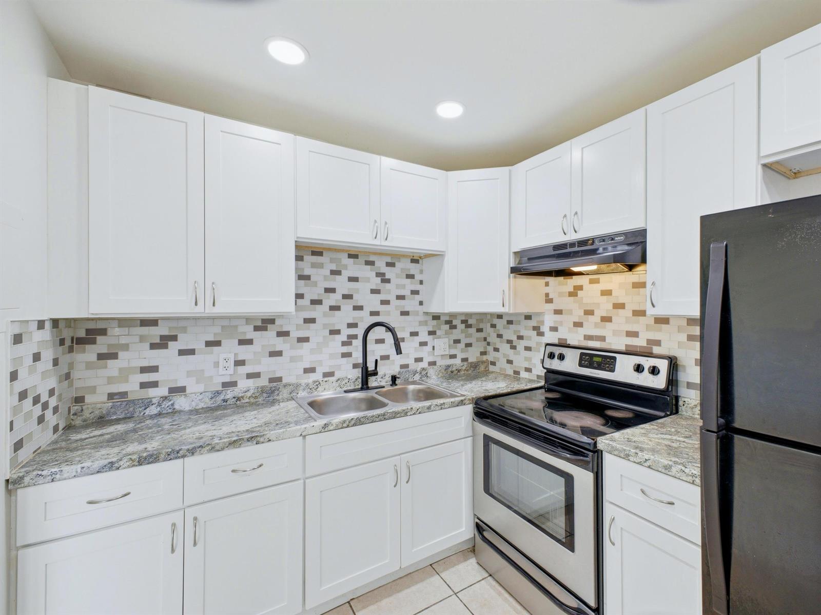 A kitchen with white cabinets, granite countertops, a tiled backsplash, and stainless steel appliances — 6289 Lear Drive # 206, Lake Worth FL 33462, LAKE WORTH, FL