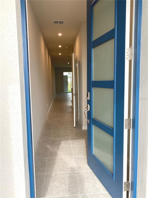 A blue front door opens into a long, tiled hallway with recessed lighting — 8850 GINKO RUN, PARRISH, FL