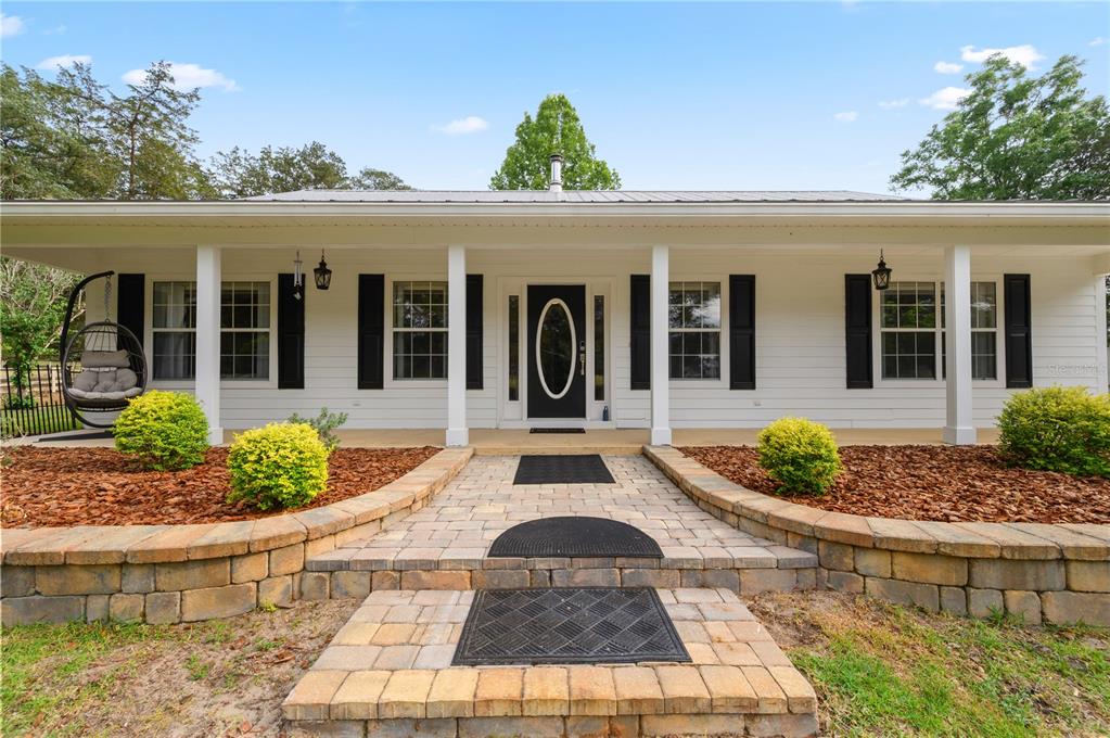 A white house with a metal roof, black shutters, and a stone retaining wall — 8822 NW 170TH STREET, ALACHUA, FL