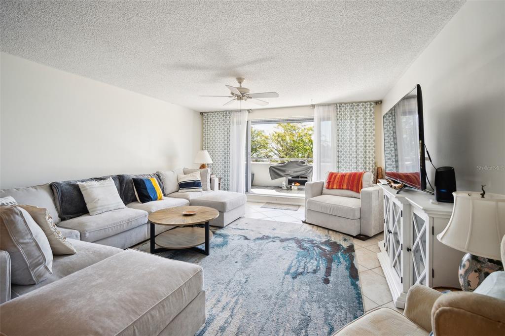 A living room features a large sectional sofa, a patterned area rug, and a balcony view — 1000 RIVERSIDE DRIVE UNIT B102, PALMETTO, FL
