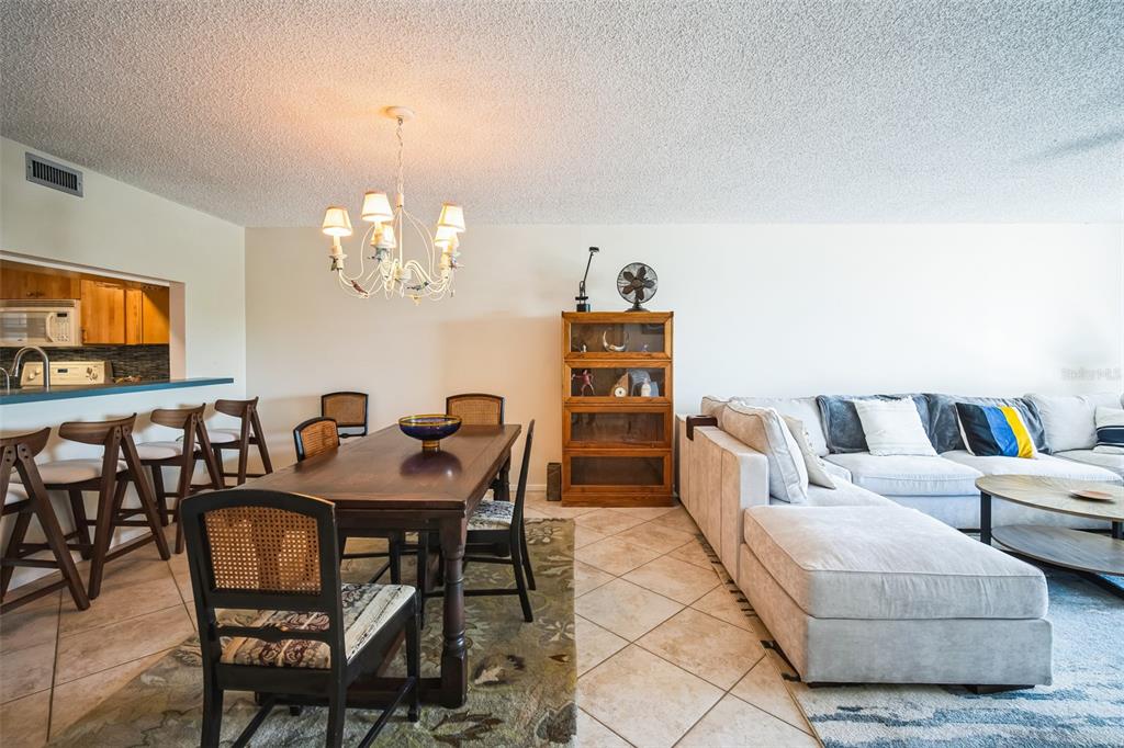 An open-concept living and dining area features tile flooring, a wooden table, and a sectional — 1000 RIVERSIDE DRIVE UNIT B102, PALMETTO, FL