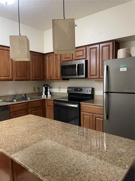 A kitchen features wood cabinets, granite countertops, stainless steel appliances, and a central island — 12544 FLORIDAYS RESORT DRIVE UNIT 612B, ORLANDO, FL