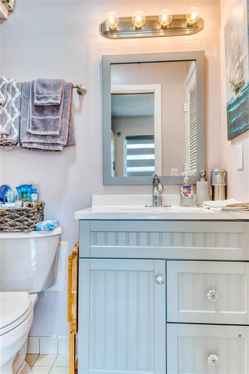 A bathroom features a light blue vanity, a gray-framed mirror, and towels hanging on the wall — 8751 Chevy Chase Drive # 150, Boca Raton FL 33433, BOCA RATON, FL